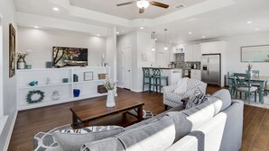 A spacious living room with a sofa, a coffee table, and a ceiling fan. There is a kitchen area with a refrigerator and a dining table. - Come stay at the Oasis by the Lake! (Canyon Lake)