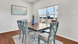 A dining area with a wooden table and blue chairs, a vase with flowers, and a view of a deck with an American flag. - Come stay at the Oasis by the Lake! (Canyon Lake)