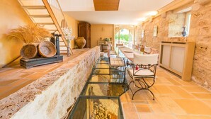 A spacious interior with a long glass water feature, wooden staircase, stone walls, and a dining area with chairs and a table.