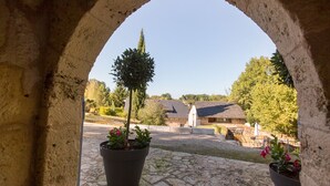 An arched stone structure with a view of a courtyard, potted plants, and buildings in the background.