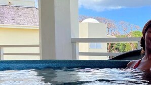 Una persona en un jacuzzi bajo una estructura cubierta con vistas a edificios y árboles.