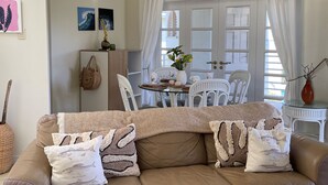 Una sala de estar acogedora con un sofá de cuero marrón, una mesita de centro de vidrio y un comedor con sillas blancas y una mesa de vidrio.