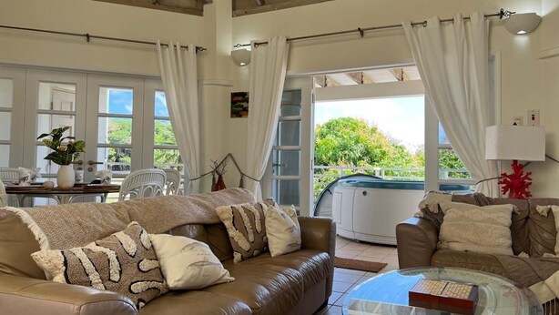 Amplio salón con sofá de cuero marrón, una mesa de centro de vidrio y vistas a un jacuzzi a través de un ventanal.