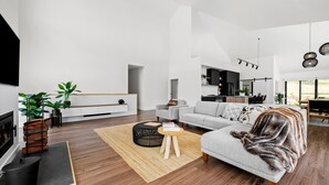Ein modernes Wohnzimmer mit Sofa, Couchtisch und Kamin. Im Hintergrund ist eine Küchenzeile erkennbar.