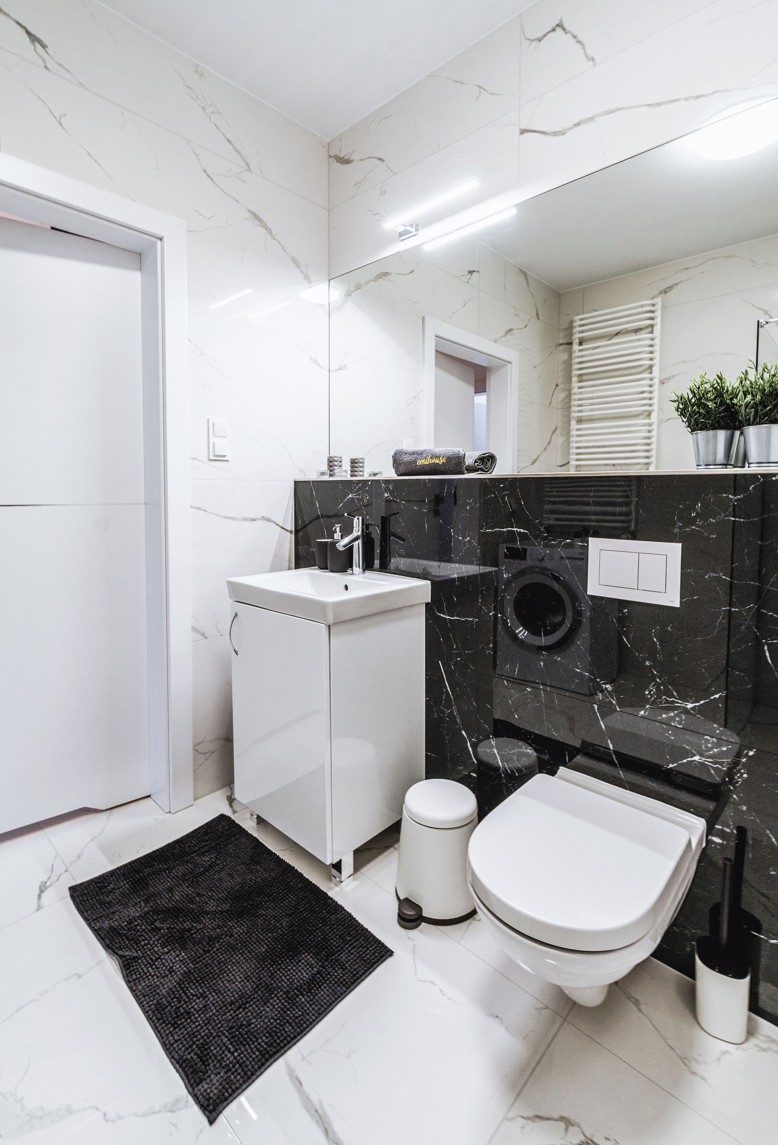 Um banheiro moderno com pia branca, paredes de mármore preto, vaso sanitário e tapete preto.
