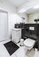 Um banheiro moderno com pia branca, paredes de mármore preto, vaso sanitário e tapete preto.