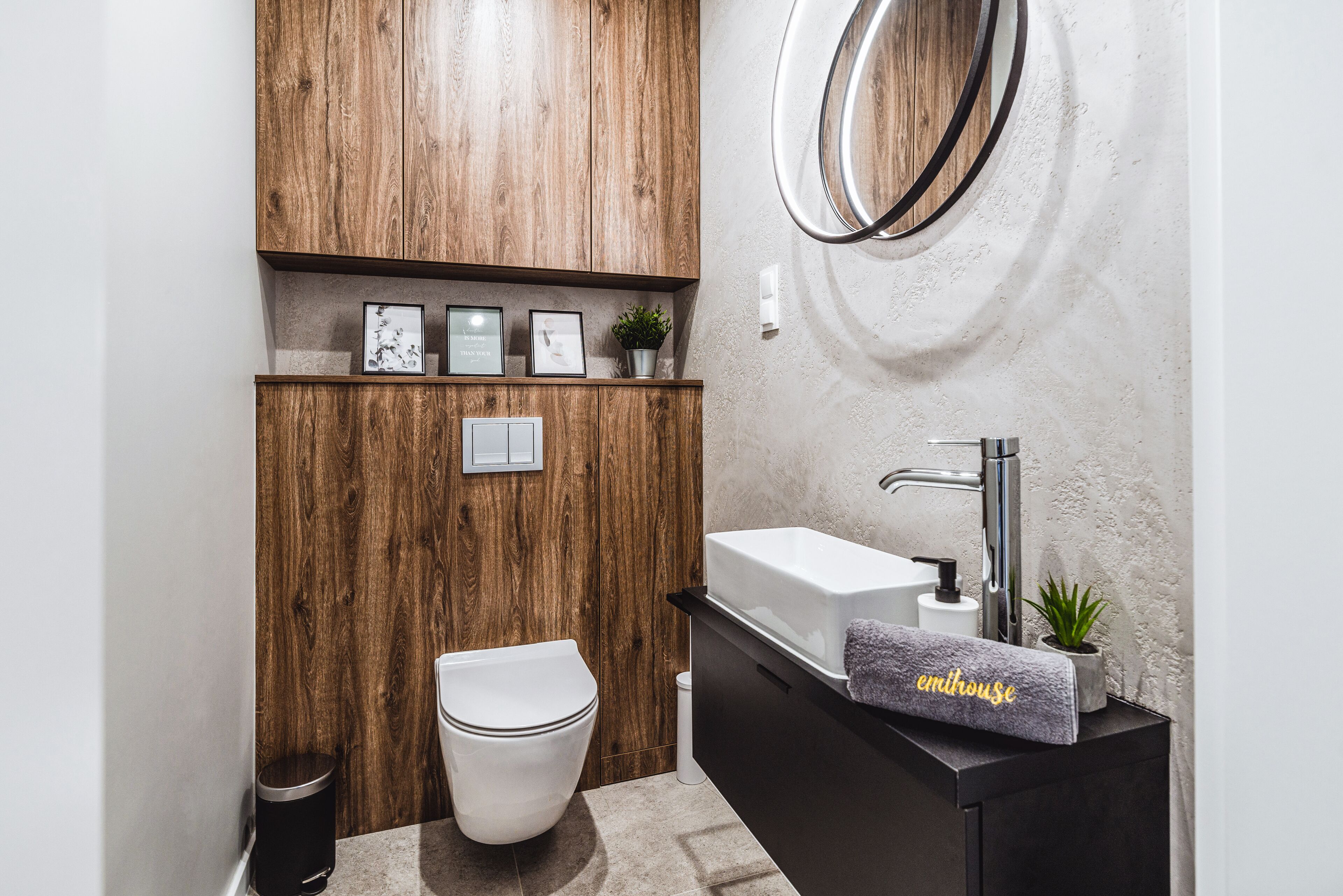 A modern bathroom with a wooden vanity, a white toilet, and a sink with a towel.