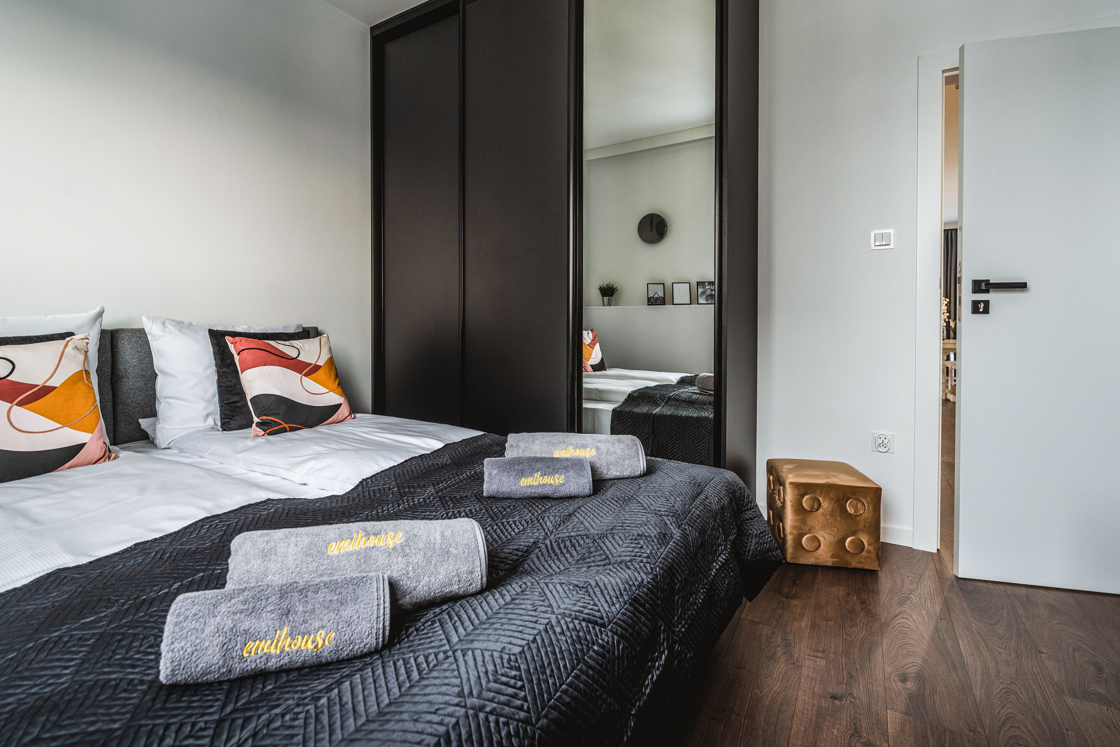 A modern hotel room with a large bed, a wardrobe, a small wooden stool, and a mirror on the wall.