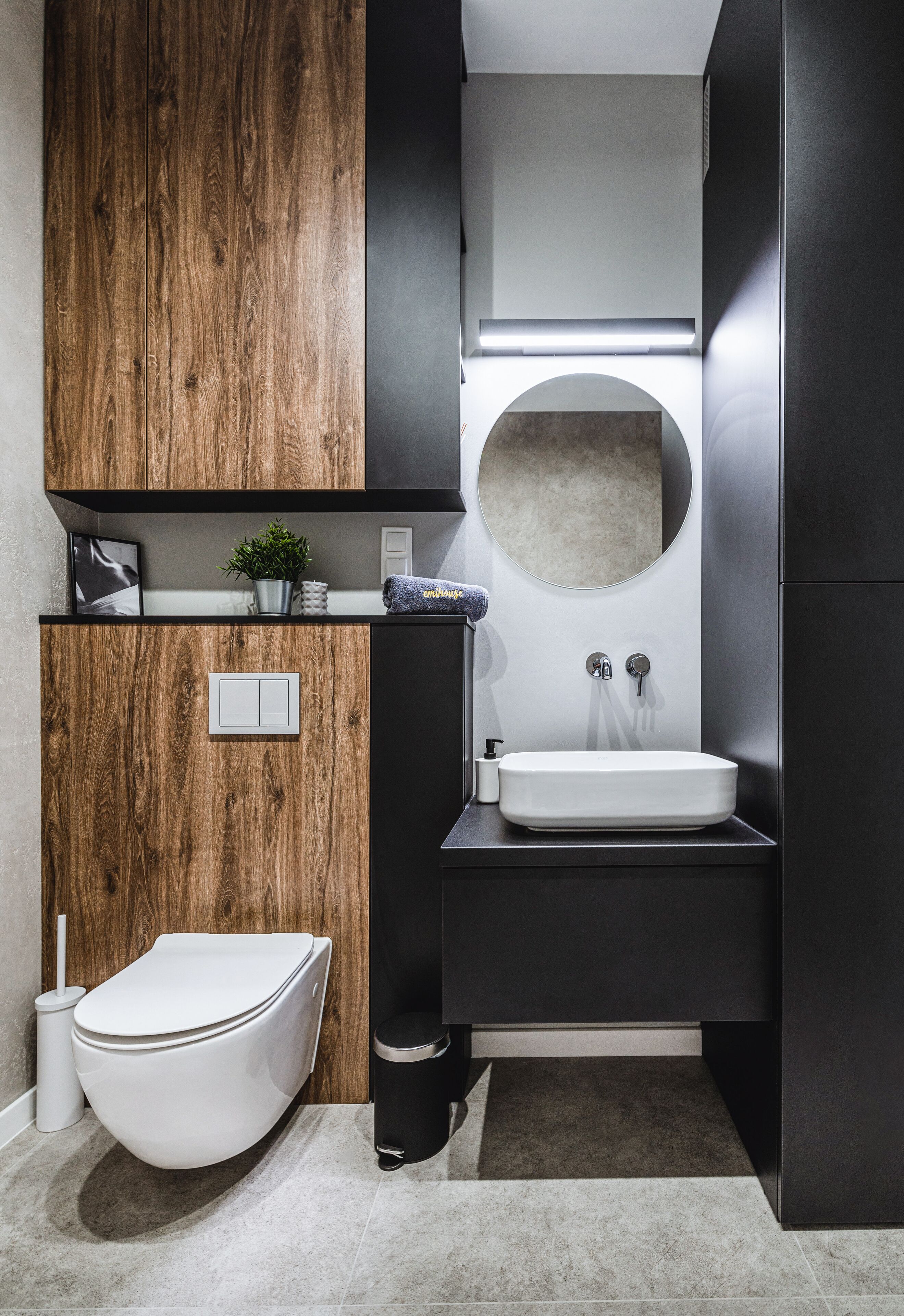 Ein modernes Badezimmer mit Waschtisch aus Holz, einem runden Spiegel, einem weißen Waschbecken und einer Toilette.