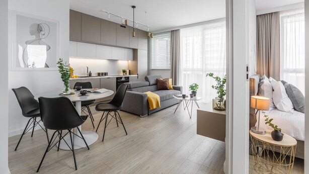 Een moderne woonkamer met een grijze bank, zwarte stoelen, een ronde eettafel en een klein bijzettafeltje met een lamp.