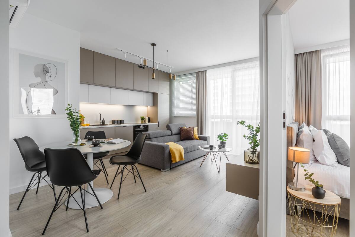 Een moderne woonkamer met een grijze bank, zwarte stoelen, een ronde eettafel en een klein bijzettafeltje met een lamp.