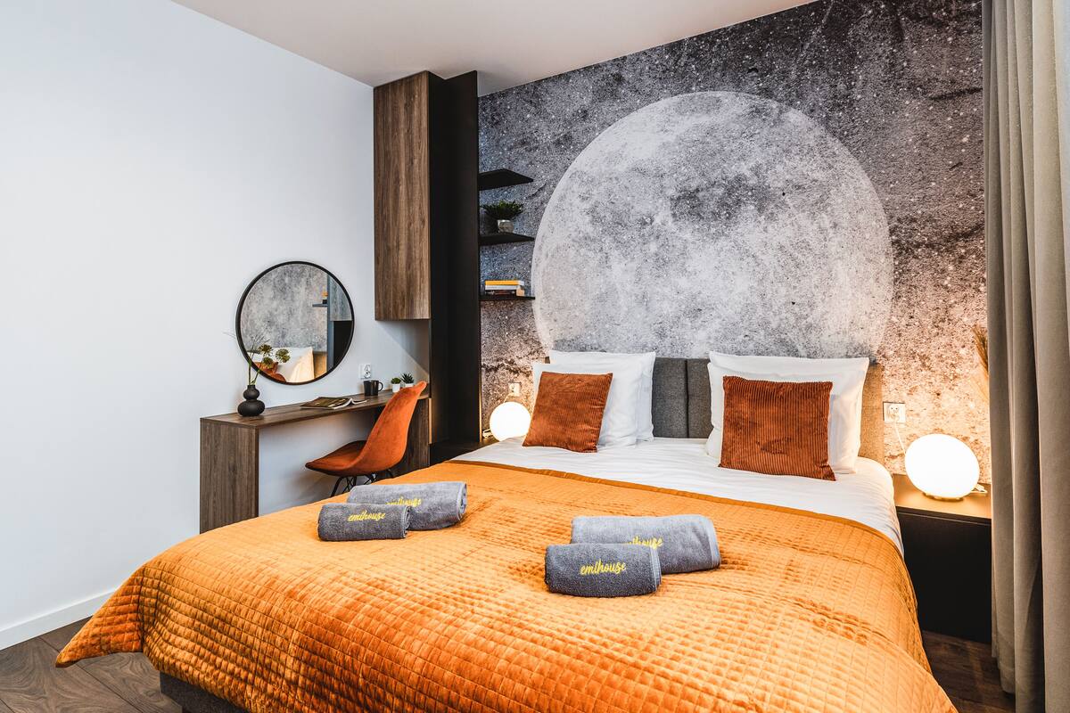 Een moderne slaapkamer met een groot bed, een ronde spiegel, een bureau en een wanddecoratie.