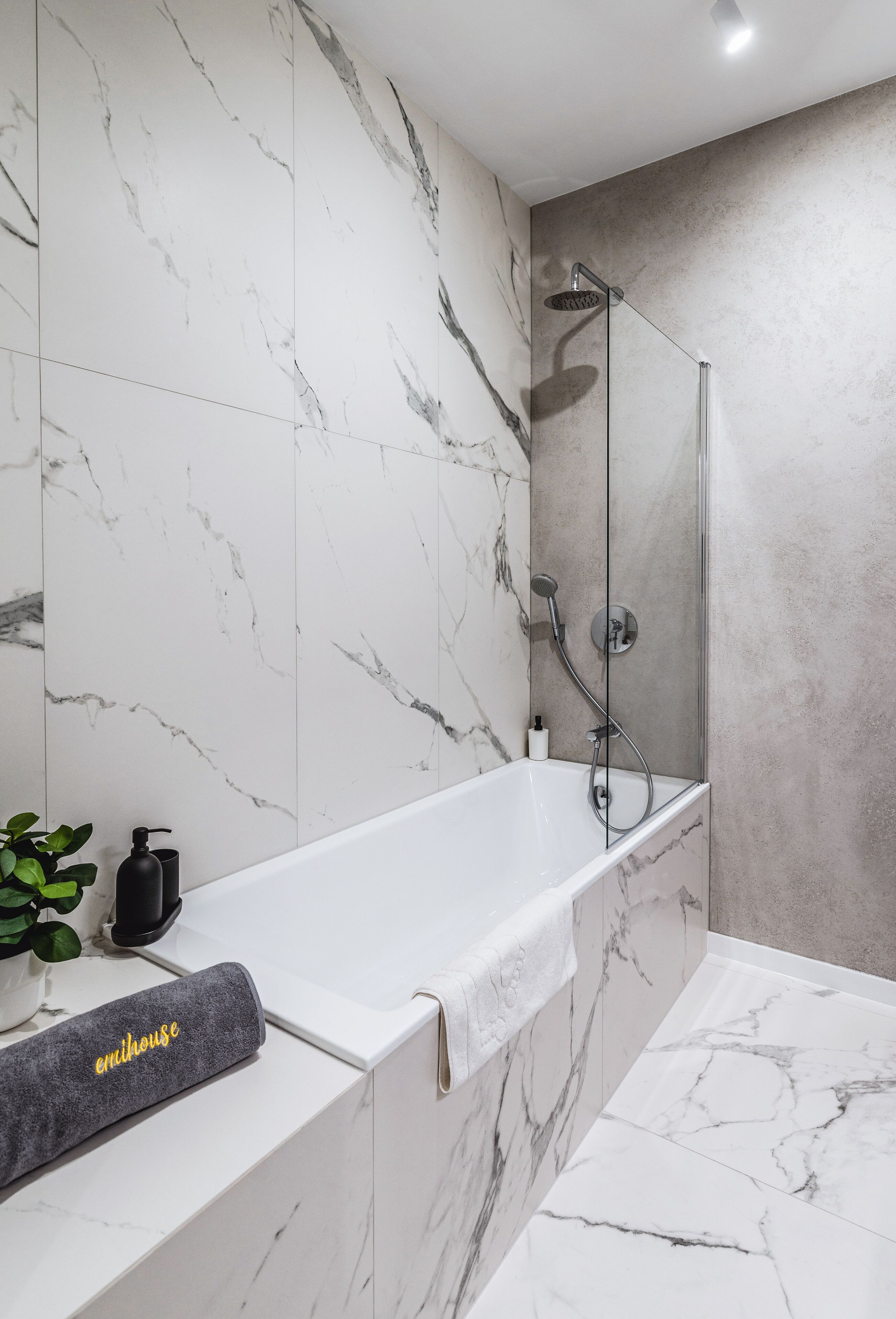 Ein modernes Badezimmer mit Marmorfliesen, einer Glaskabinentrennwand für die Dusche und einer weißen Badewanne.