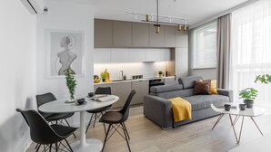 Een moderne woonkamer met een grijze bank, een ronde eettafel en een keuken met grijze kasten en een wit aanrecht.