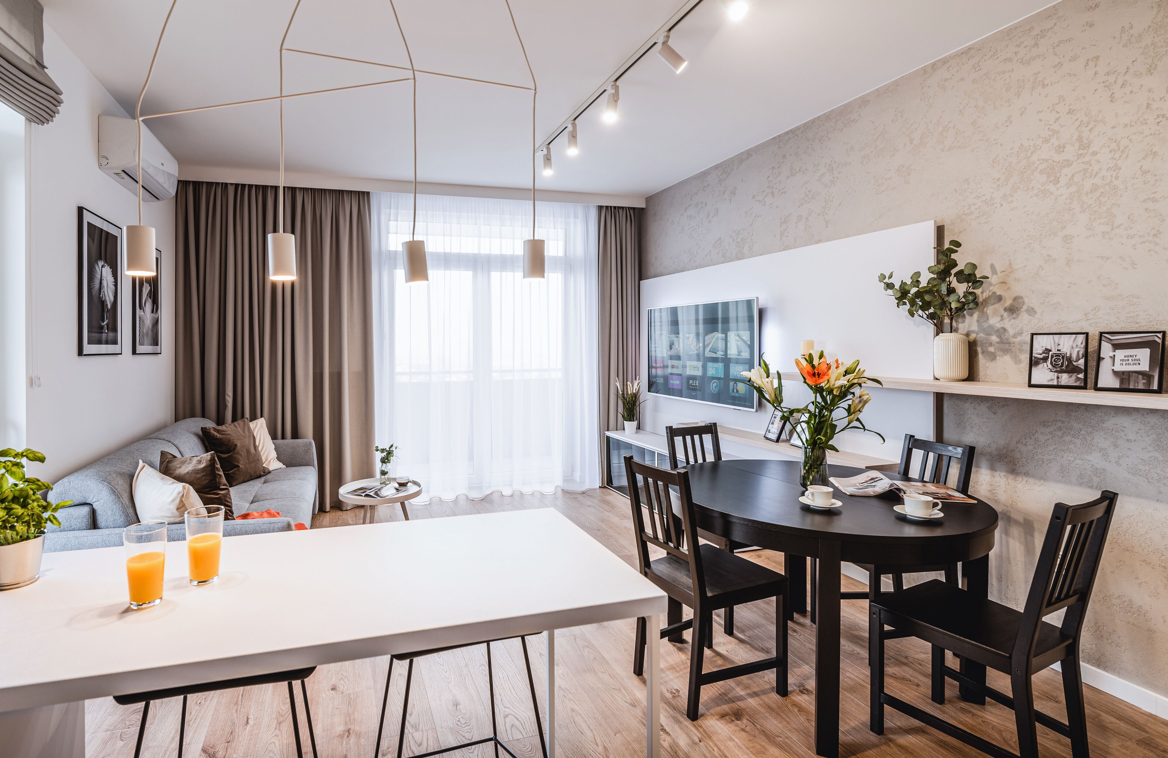 Un salon moderne avec un canapé, une table à manger et des chaises, et un téléviseur fixé au mur.