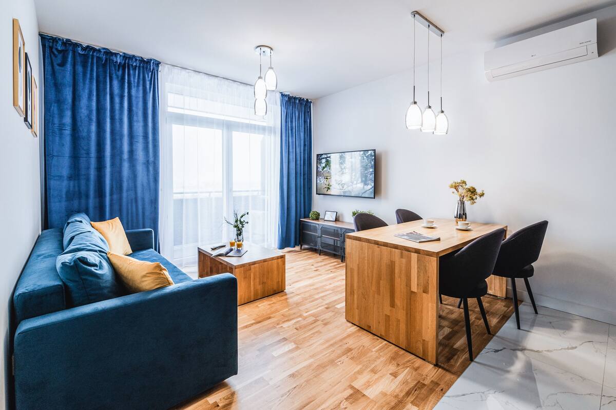 Een moderne woonkamer met een blauwe bank, een houten salontafel en een eethoek met een houten tafel en stoelen.