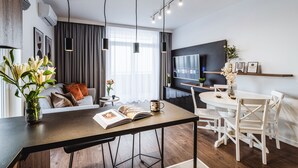 Een moderne woonkamer met een eethoek, een flatscreen televisie aan de muur en een groot raam met gordijnen.