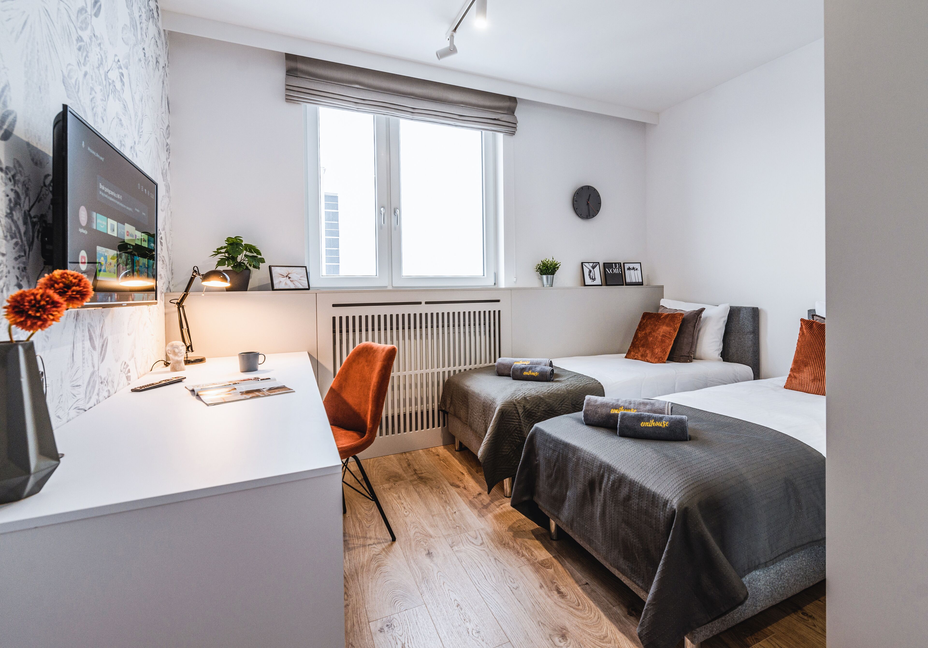 Ein modernes Hotelzimmer mit großem Fenster, einem Schreibtisch mit Computer, zwei Betten und einer Heizung.