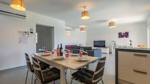 A modern dining area with a table set for four, a sofa, a TV, and a kitchen area with cabinets.