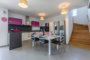 Una cocina moderna con comedor, que incluye una isla central, luces colgantes y una escalera que sube a un nivel superior.