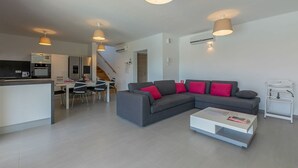 A modern living room with a grey sectional sofa, a white coffee table, and a dining area with a white table and chairs.
