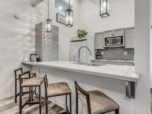 Una cucina moderna con un piano di lavoro bianco, sgabelli da bar, un lavandino e un forno a microonde.