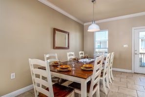 A dining area with a wooden table set for six, white chairs, and a pendant light.