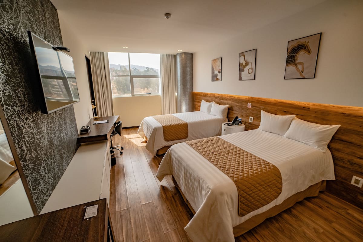A hotel room with two beds, a desk, a TV, and a window with a view.