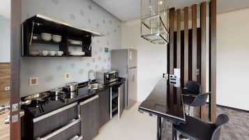A modern kitchen with a black countertop, stainless steel appliances, and a built-in oven. There is a dining area with a black chair and a glass table.