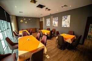 Un comedor con varias mesas y sillas, piso de madera y obras de arte en las paredes.