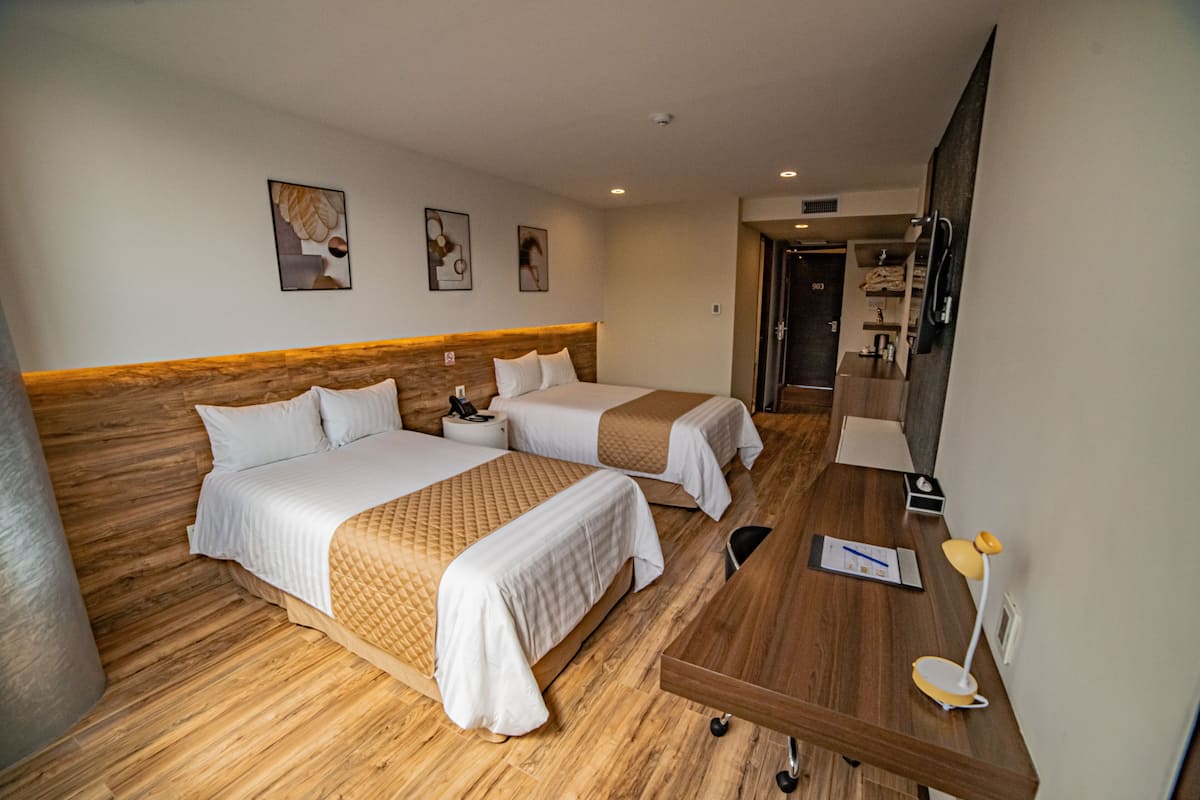 A hotel room with two beds, a wooden headboard, a desk with a lamp, and a mirror.