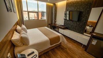 A hotel room with a bed, bedside table, desk, TV, and a view of the city.