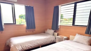 A hotel room with two single beds, a small bedside table with a lamp, and large windows with curtains. - AZ Hotel Inn Amamimanya (Amami)