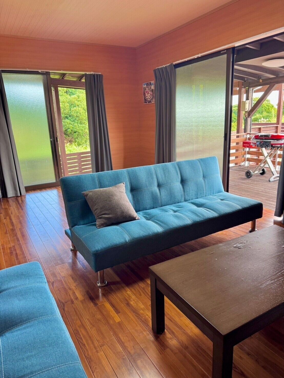 A room with a blue sofa, a wooden table, and a view of a barbecue grill outside.