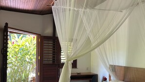 A room with a bed under a mosquito net, a wooden ceiling, and a view of greenery outside. - POUSADA HORIZONTE AZUL (Cairu)