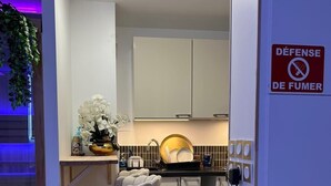 A modern kitchen with white cabinets, a bar stool, and a 'DEFENSE DE FUMER' sign. - Superb sauna jacuzzi apartment Luxury&Spa (Herblay)