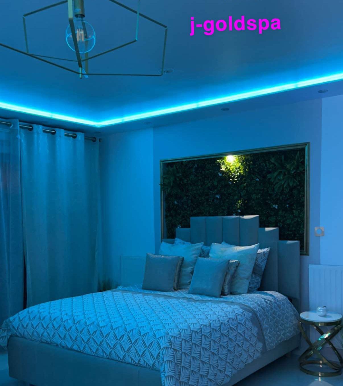 A modern bedroom with a king-sized bed, blue LED lighting, and a geometric ceiling design.