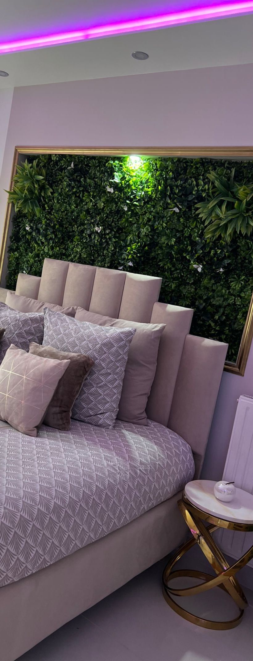 A modern bedroom with a large bed, a green wall with foliage, and a small bedside table.