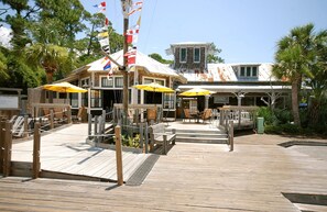 Relax on the outdoor deck with comfortable seating and tables under shaded umbrellas, surrounded by palm trees and the ocean.