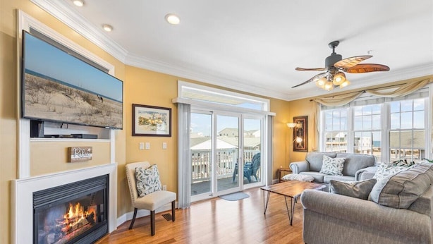 A living room with a fireplace, a ceiling fan, and a large window overlooking a balcony.