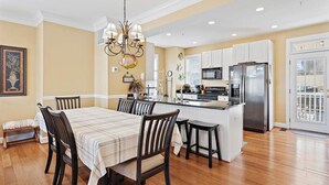 A modern kitchen with a central island, white cabinetry, stainless steel appliances, and a dining area with a table and chairs.