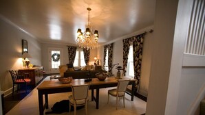 Un comedor con una mesa de madera, cuatro sillas, una araña y una cocina al fondo.