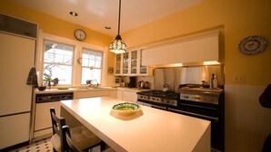Una cocina con una isla central, muebles blancos, una estufa y una lámpara colgante.