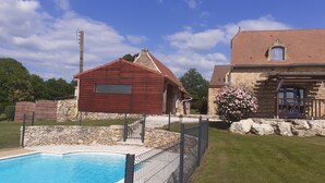 Zona de piscina con muro de piedra y edificio de madera con techo rojo.
