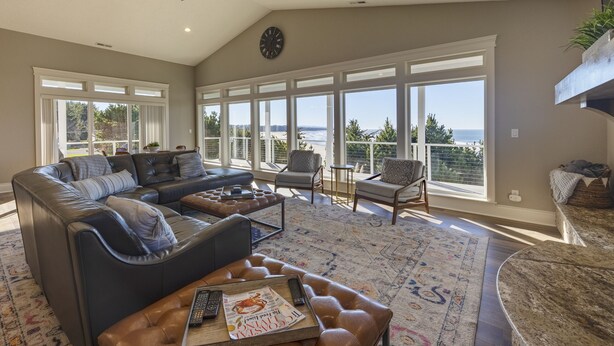 A spacious living room with a large sectional sofa, a coffee table, and a view of the ocean through large windows. - Point Break at Agate Beach, Sleeps 12, Oceanfront, Loft, Game Room, Hot Tub, Beach Access, BBQ (Newport)