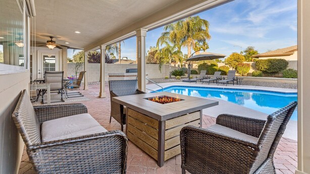 A covered patio area with wicker furniture, a pool, and a fire pit.