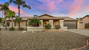 A residential house with a driveway, palm trees, and a gravel lawn.