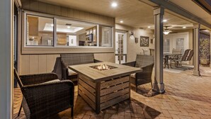 An outdoor patio with wicker furniture, a central fire pit, and a view into the adjacent kitchen area.