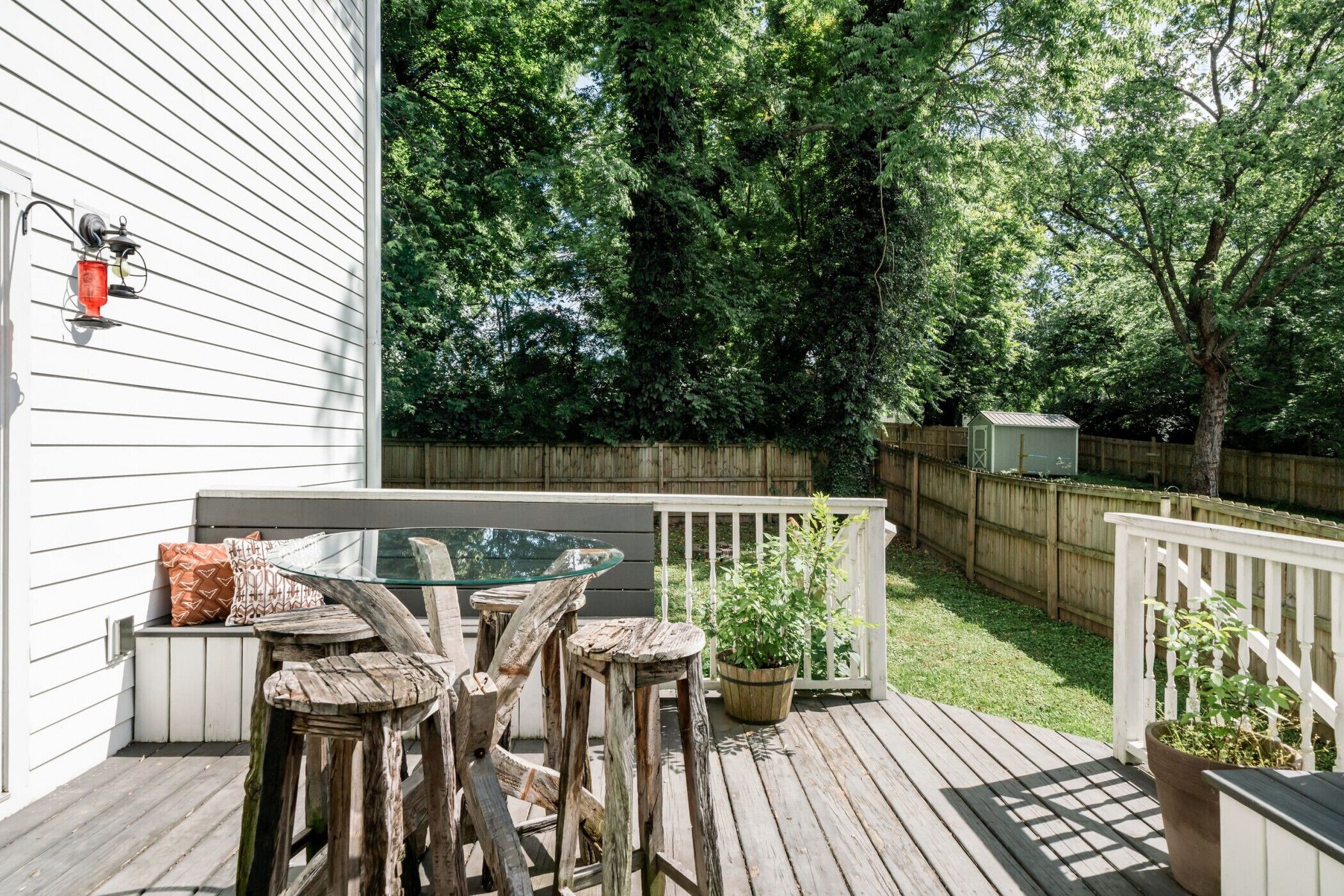 A wooden deck with a glass table and stools, surrounded by white railings and a wooden fence.