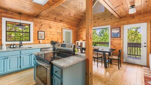 Una cabaña de madera con cocina, comedor y balcón con vistas a árboles.
